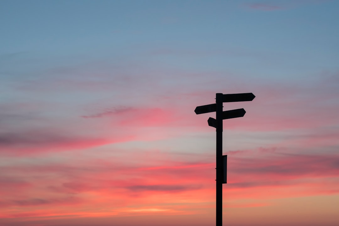 Silhouette of a directional signpost against a colorful sunset sky